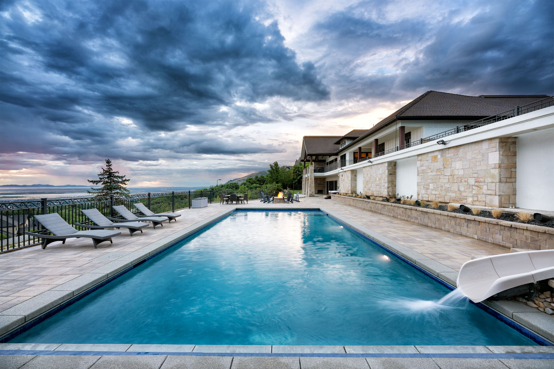 Swimming pool with waterslide next to large house overlooking valley - Precision Pools