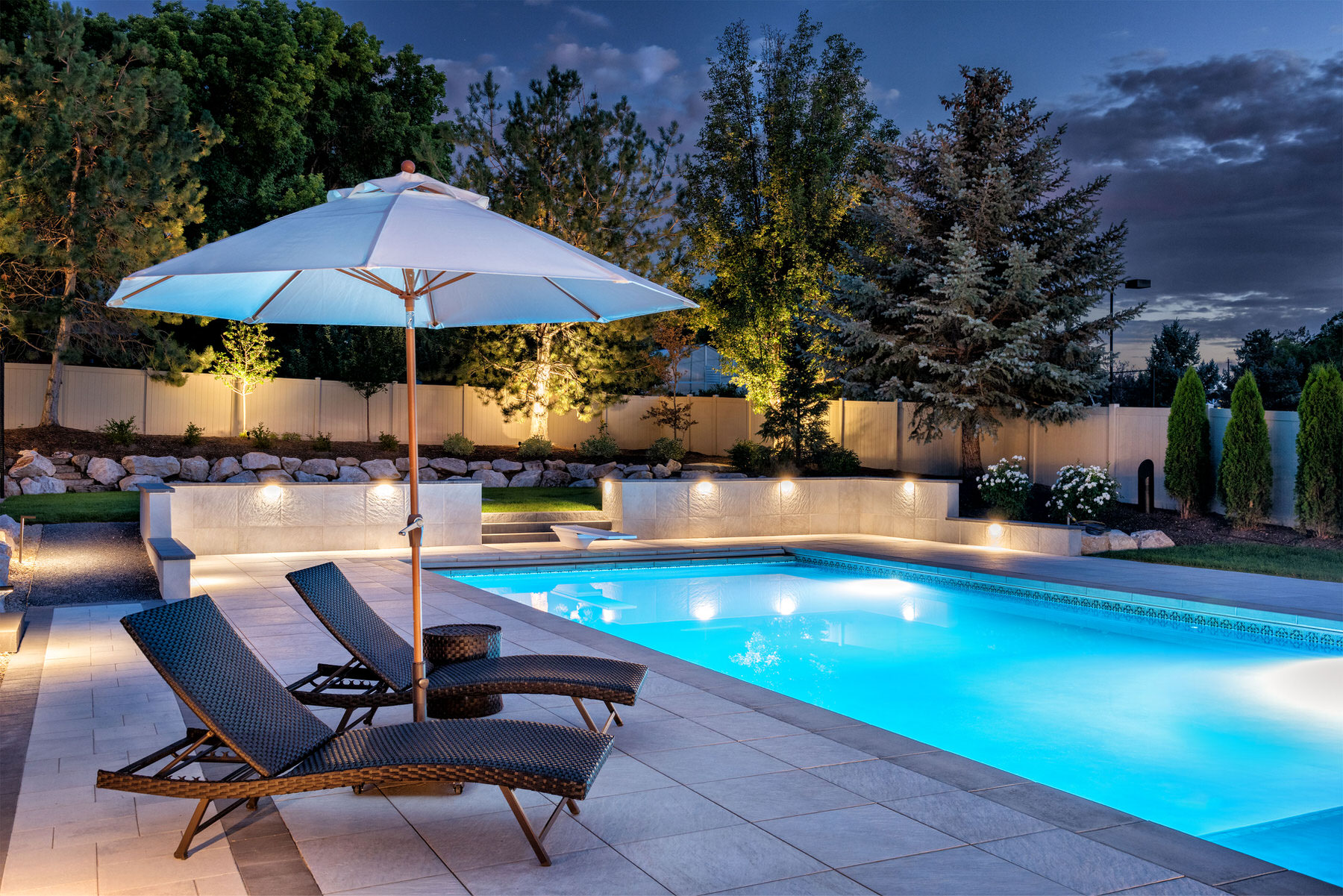 Swimming pool with lights on at night in private garden with sun beds - Precision Pools