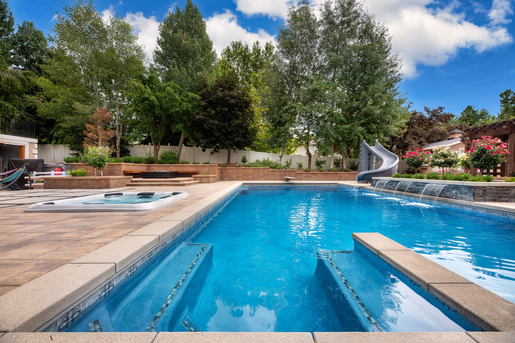 Swimming pool with slide and waterfall surrounded by garden trees