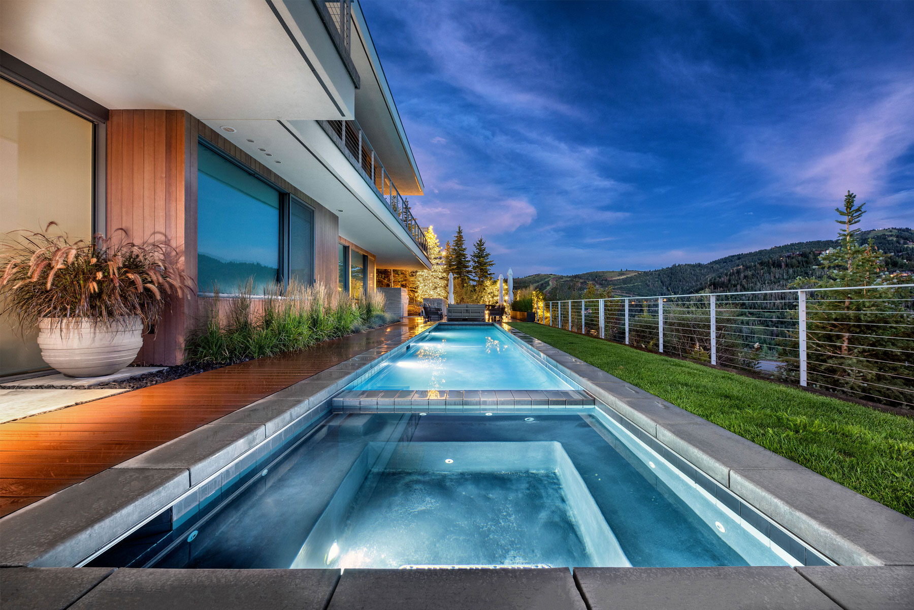 Swimming Pool with spa pool next to large house overlooking hillside at night - Precision Pools